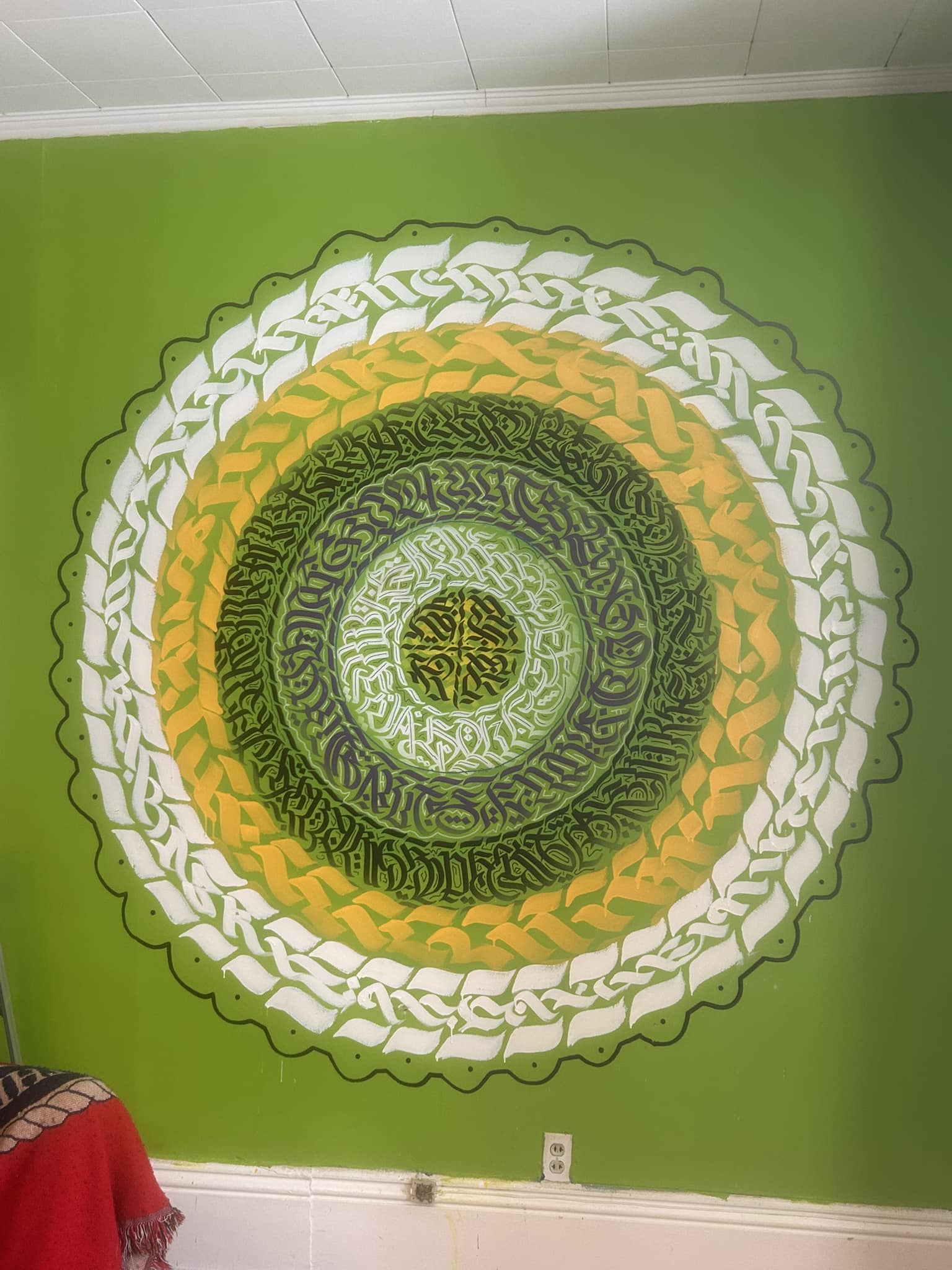 Calligraffiti spiral mandala in gold and green on green wall
