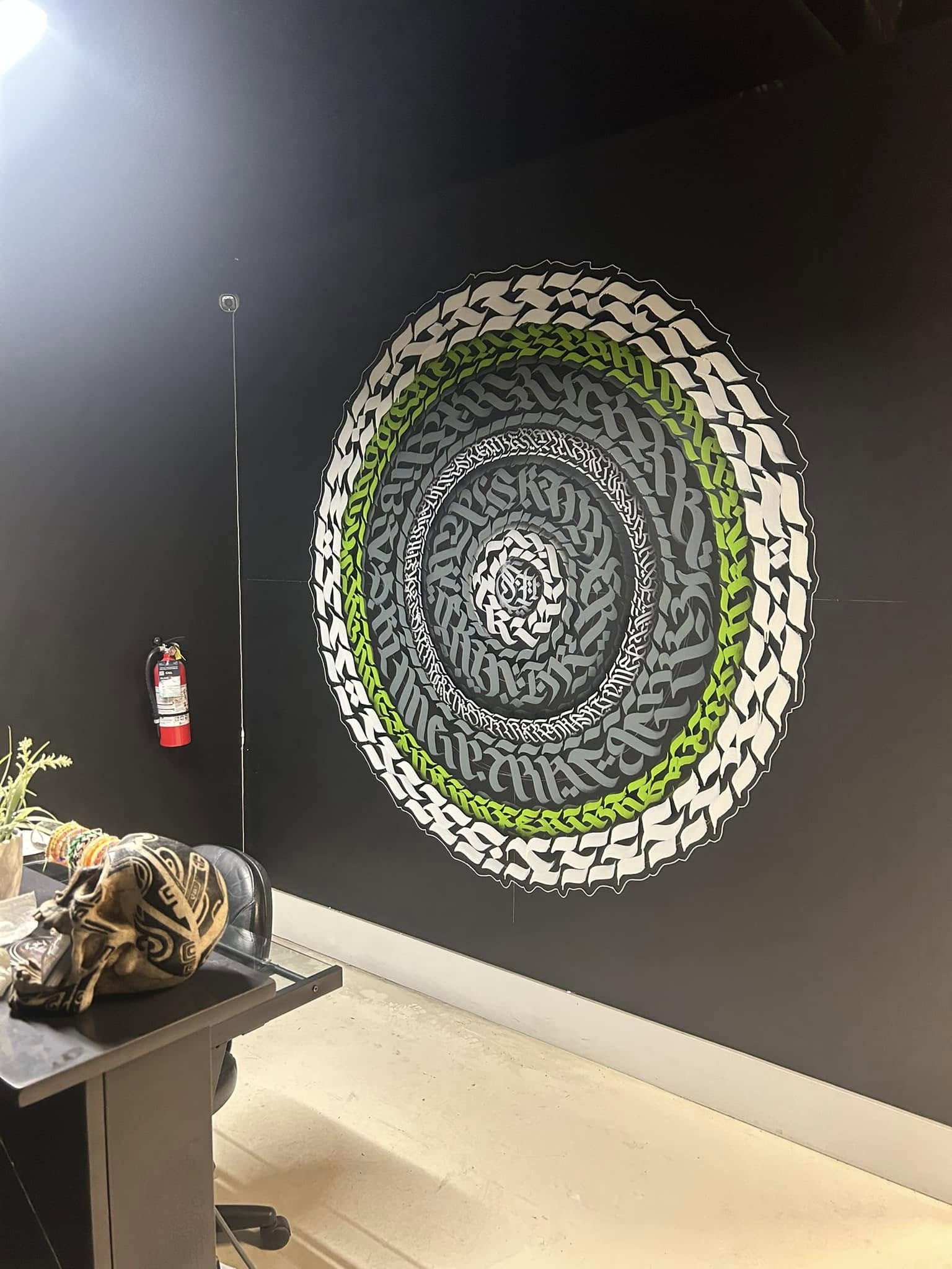 Calligraffiti spiral mandala in green and white on dark wall